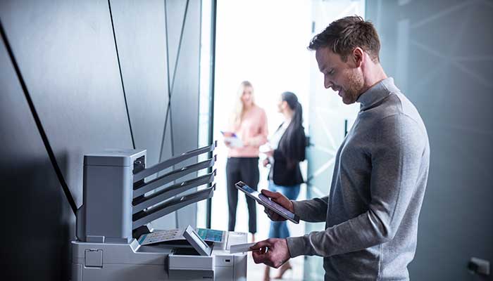 Uomo con carta NFC vicino a stampante, con tablet in mano, persone sullo sfondo